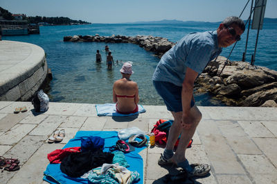 People standing on retaining wall by sea