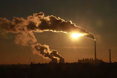 Silhouette of factory against sky during sunset