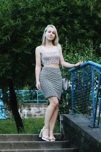 Portrait of beautiful young woman standing on steps by railing at park