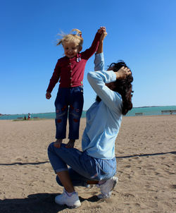 Mother and daughter playing at beach against clear sky