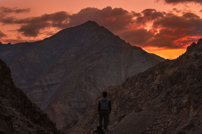 Rear view of man standing on mountain against sunset sky