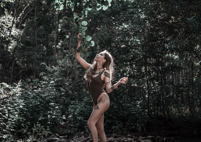 Full length of woman standing by tree in forest