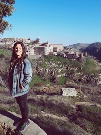 Portrait of beautiful woman standing on retaining wall against blue sky