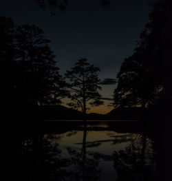 Silhouette trees by lake against sky at night