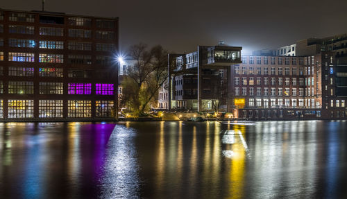 Illuminated buildings by river against sky in city at night