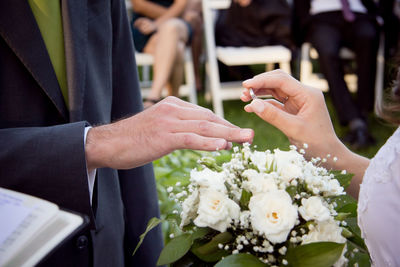 Midsection of bride holding ring by bridegroom during wedding ceremony
