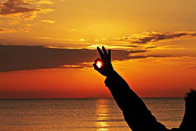 Optical illusion of person holding sun at beach during sunset