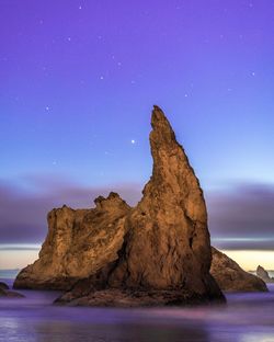 Rock formation in sea against sky at dusk