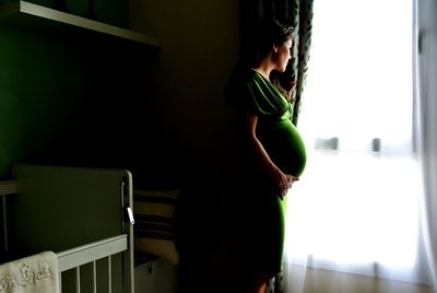 Side view of pregnant woman looking through window at home