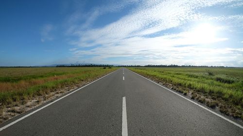 Empty road amidst field against sky