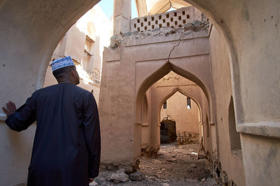 Oman. rear view of man standing at entrance of historic building