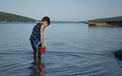 Boy with red bucket standing in lake