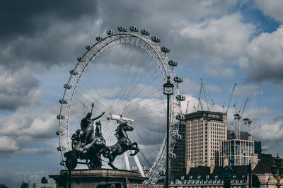 Low angle view of ferris wheel against cloudy sky