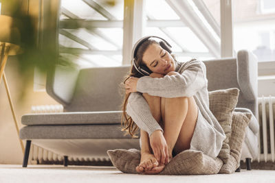 Woman with closed eyes sitting on cushion on floor wearing headphones