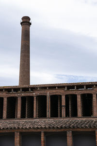 Low angle view of factory against cloudy sky