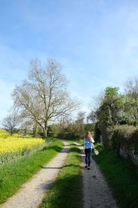 Rear view of woman walking on dirt road against sky