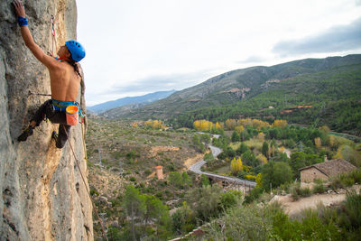 Shirtless man rock climbing against sky