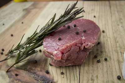 Close-up of meat with black peppercorn and rosemary leaves on table