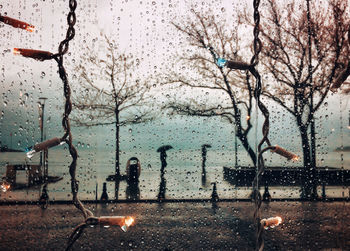 Focus on raindrops with people walking with umbrellas on the coastline.