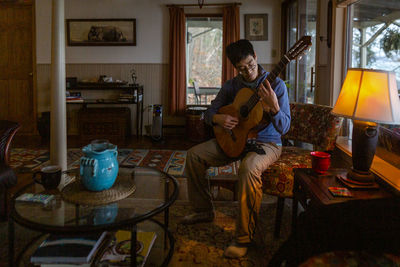 Portrait of a man playing guitar by himself in an eclectic home