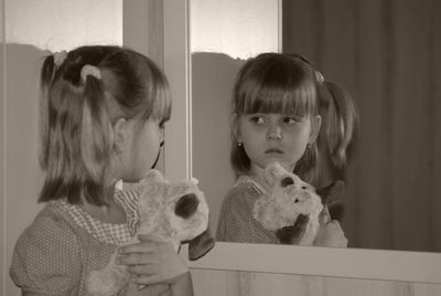 Girl holding stuffed toy looking at mirror reflection