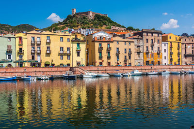 Boats moored in river by buildings against sky