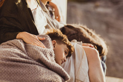 Tired son sleeping on mother's lap during summer