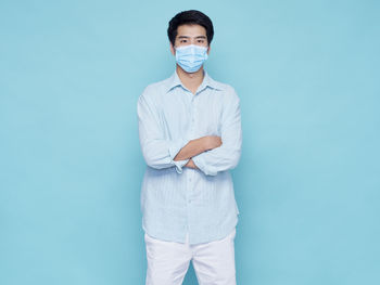 Portrait of young man wearing mask standing against blue background