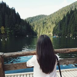 Rear view of woman standing by lake against sky