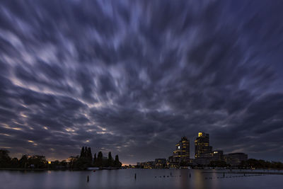 View of illuminated buildings by river against cloudy sky