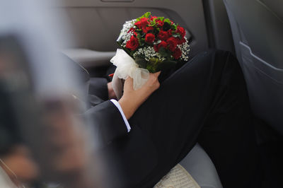Midsection of groom with bouquet sitting in car