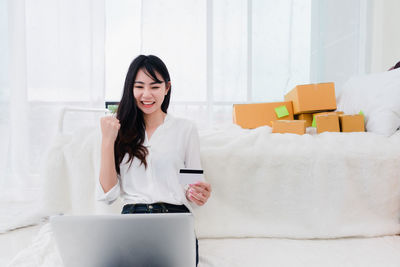 Young woman using phone while standing on sofa