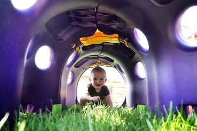 A small boy laughs as he crawls through the colorful tunnel at the playground.
