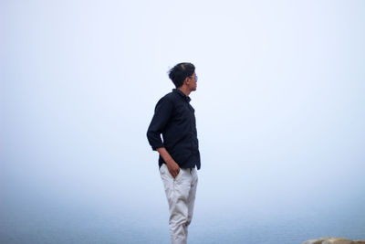 Side view of young man looking at sea against clear sky