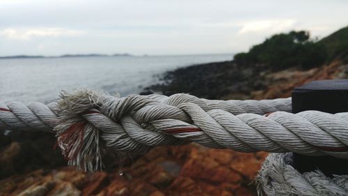 Close-up of rope tied up at beach against cloudy sky