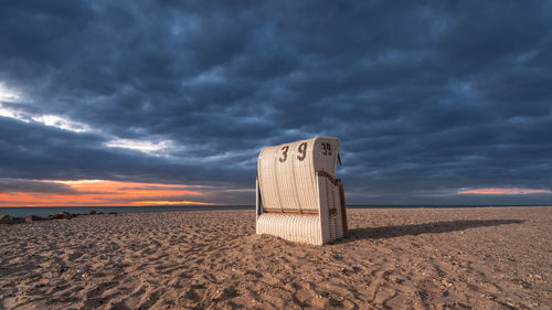 Hooded beach chair on sand against dramatic sky