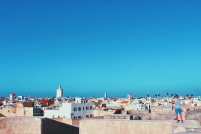 Rear view of man standing on rooftop against clear blue sky