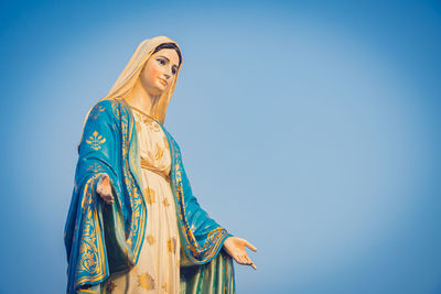 Low angle view of woman standing against clear blue sky