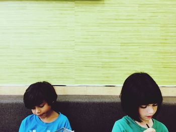 Siblings sitting on sofa against green wall