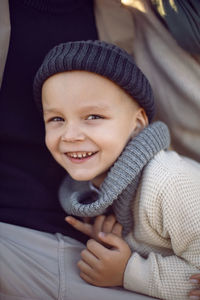 Portrait of a boy child in autumn in a knitted hat sitting with his parents in a field