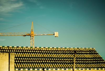 Low angle view of crane against building against clear blue sky