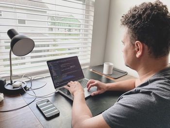 Side view of man working by using laptop at home