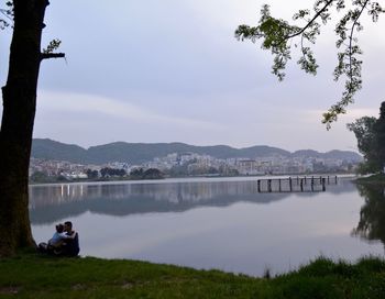 Couple romancing by lake against cloudy sky