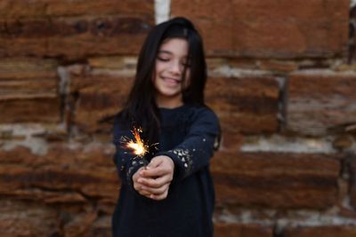 Cheerful girl playing while standing against brick wall