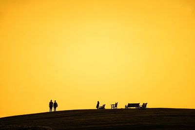 Silhouette people walking on road against orange sky