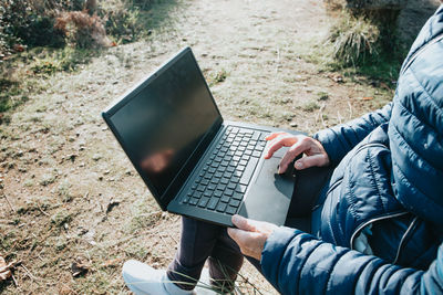 Midsection of woman using laptop while sitting on field