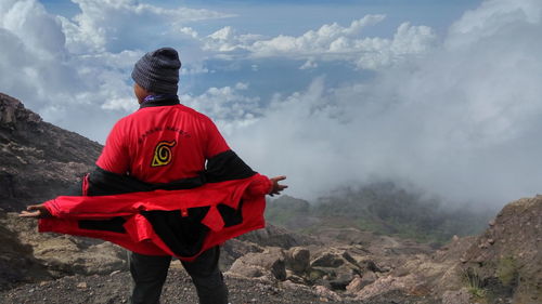 Rear view of man standing on mountain against sky