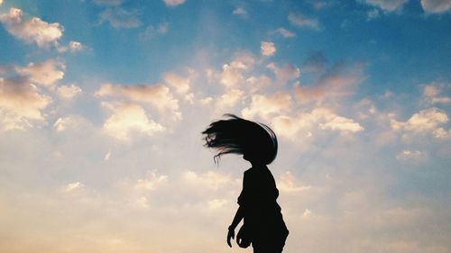 Silhouette woman tossing hair against cloudy sky during sunrise