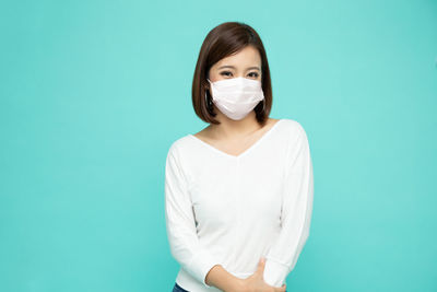 Portrait of beautiful young woman wearing mask against blue background