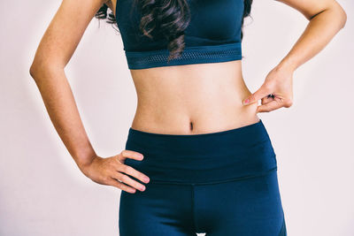 Midsection of woman holding belly while standing against white background